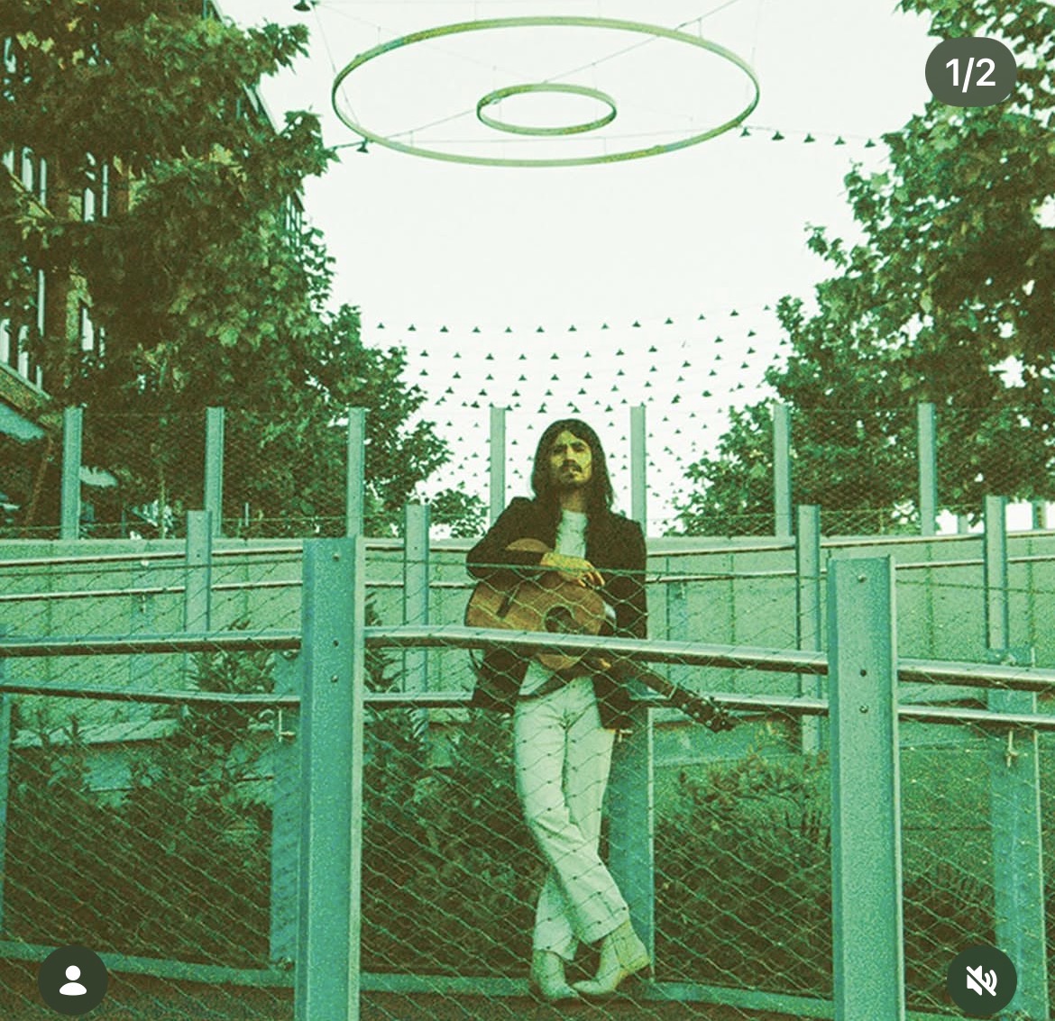 Prieto Bosques standing with a guitar beneath a circular structure.